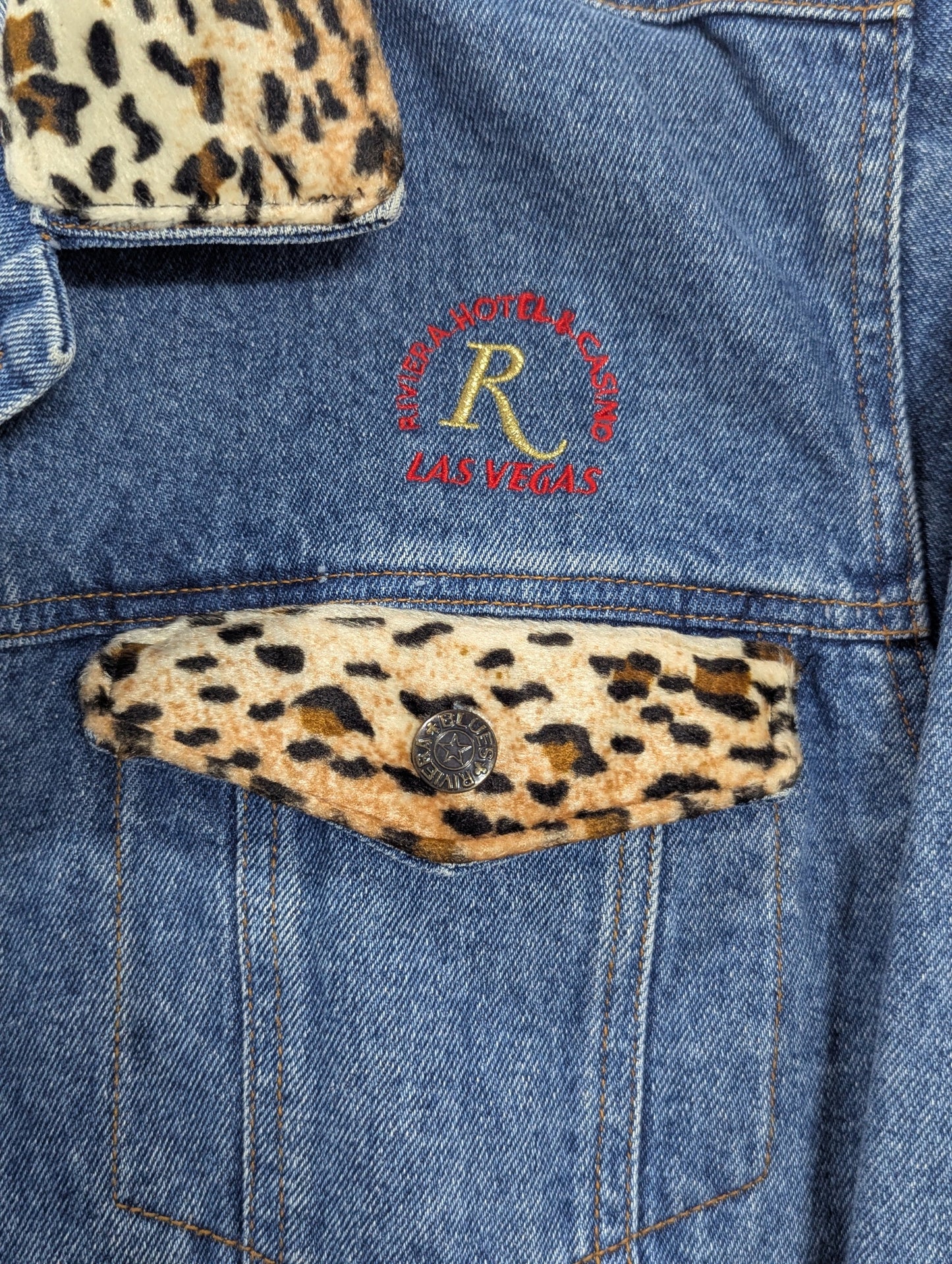 Close-up detail shot of the vibrant, custom embroidered Riviera Hotel Las Vegas casino logo on heavy-duty blue denim fabric with a vintage indie vibe.