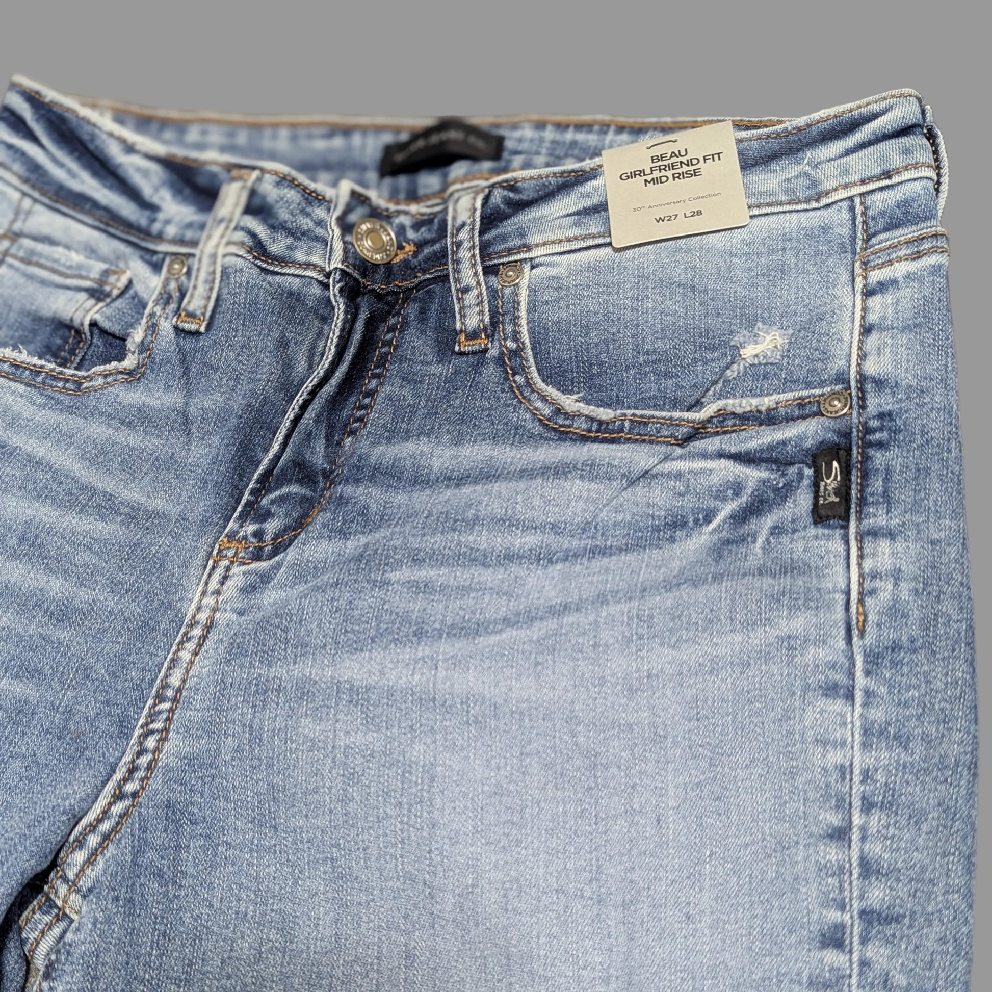 Up close view of Silver Jeans "Beau" girlfriend fit mid-rise denim jeans in a medium wash with distressed details, highlighting a vintage thrift aesthetic.