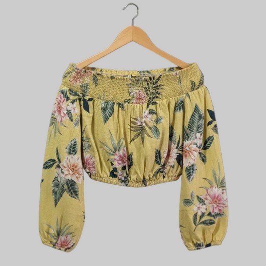 Close-up view of the bodice of a yellow floral Guess crop top, highlighting the gathered elastic, off-the-shoulder neckline, and the lightweight linen-rayon blend fabric texture.