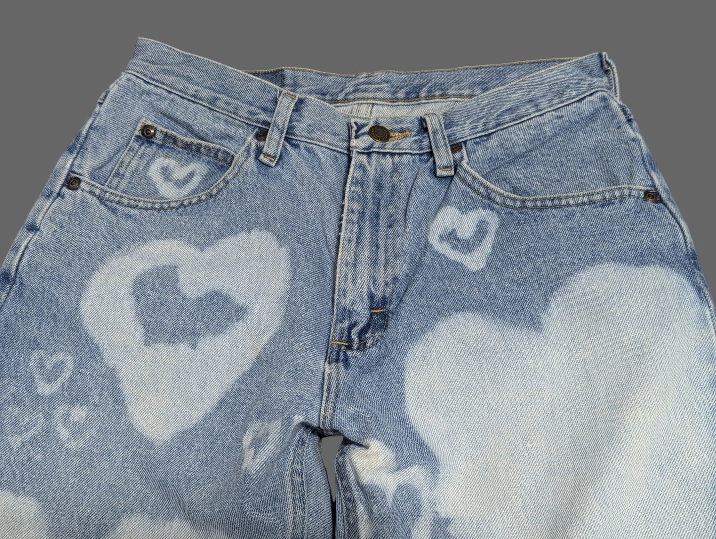 Close up view of light wash vintage Wrangler straight leg denim jeans with a custom white bleached heart pattern down both legs.