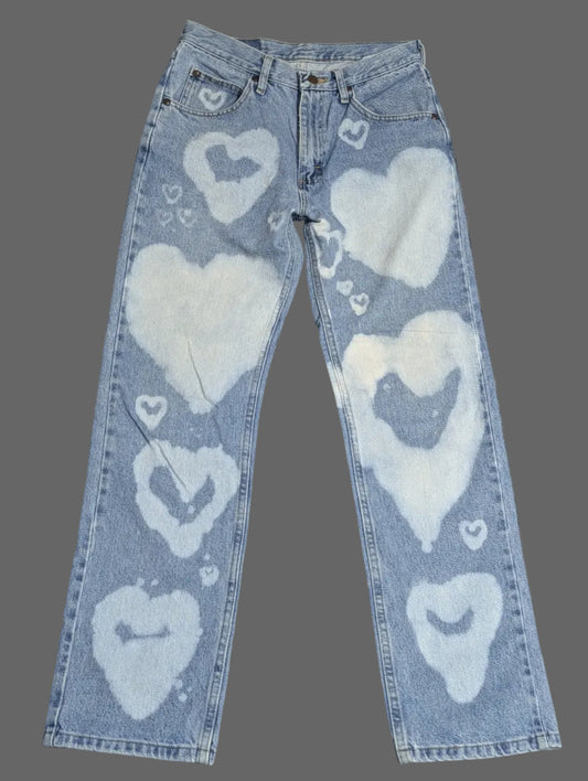 Front view of light wash vintage Wrangler straight leg denim jeans with a custom white bleached heart pattern down both legs.