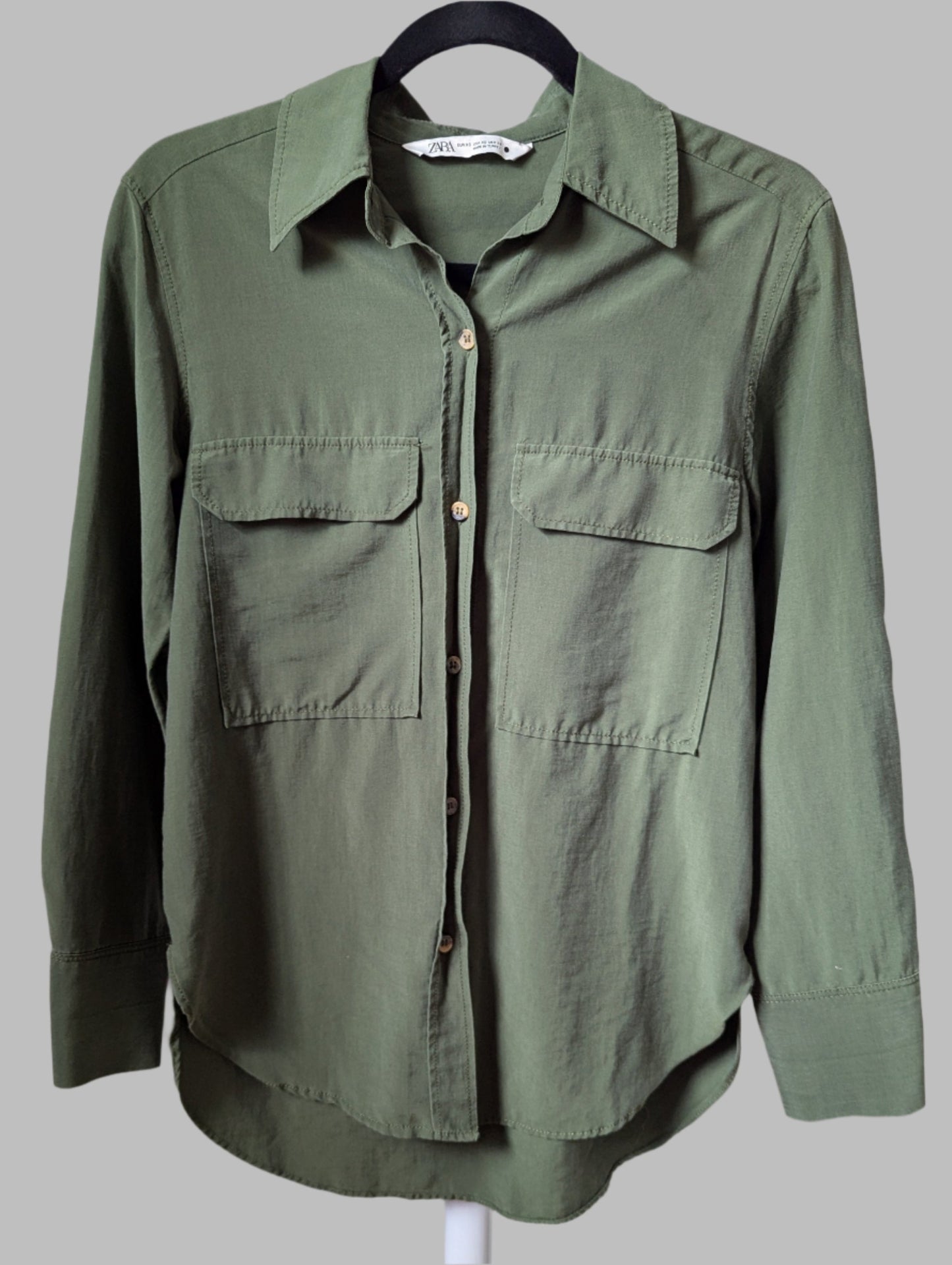 Angled view of a lightweight green Zara button-up shirt, showing the fluid drape of the lyocell fabric.