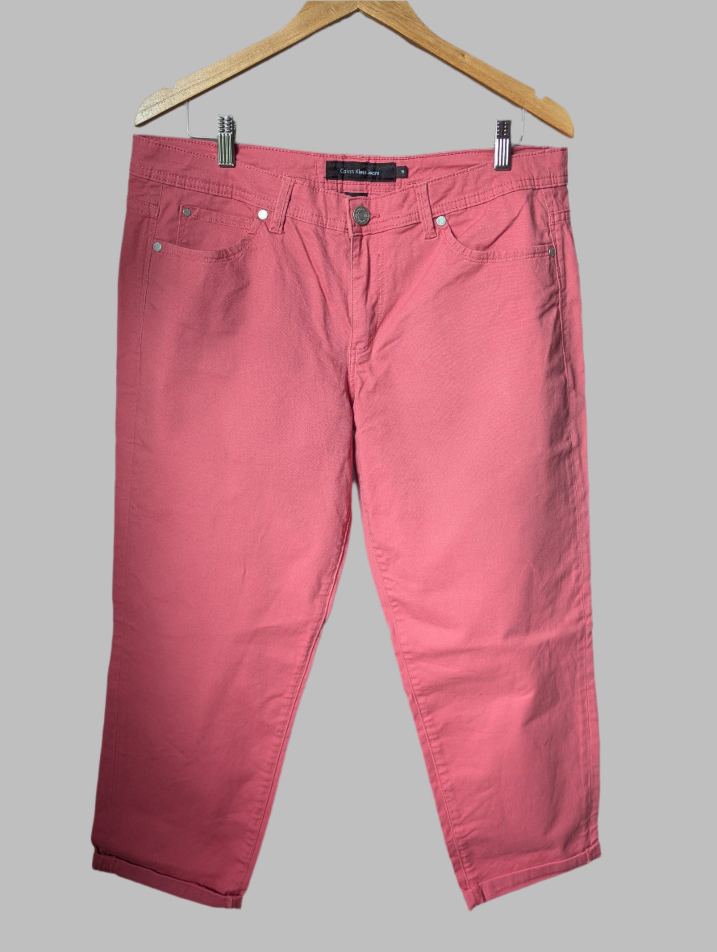 Front view of salmon pink Calvin Klein high-rise cropped jeans hanging on a wooden hanger.