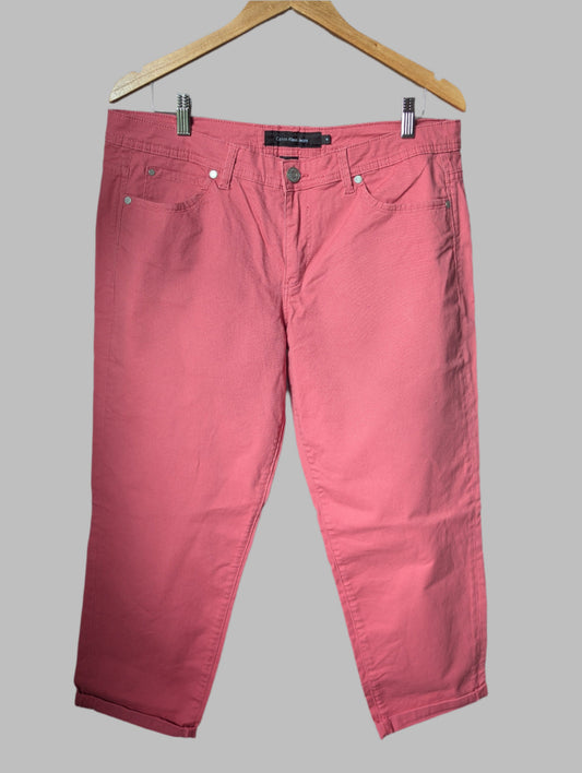 Front view of salmon pink Calvin Klein high-rise cropped jeans hanging on a wooden hanger.
