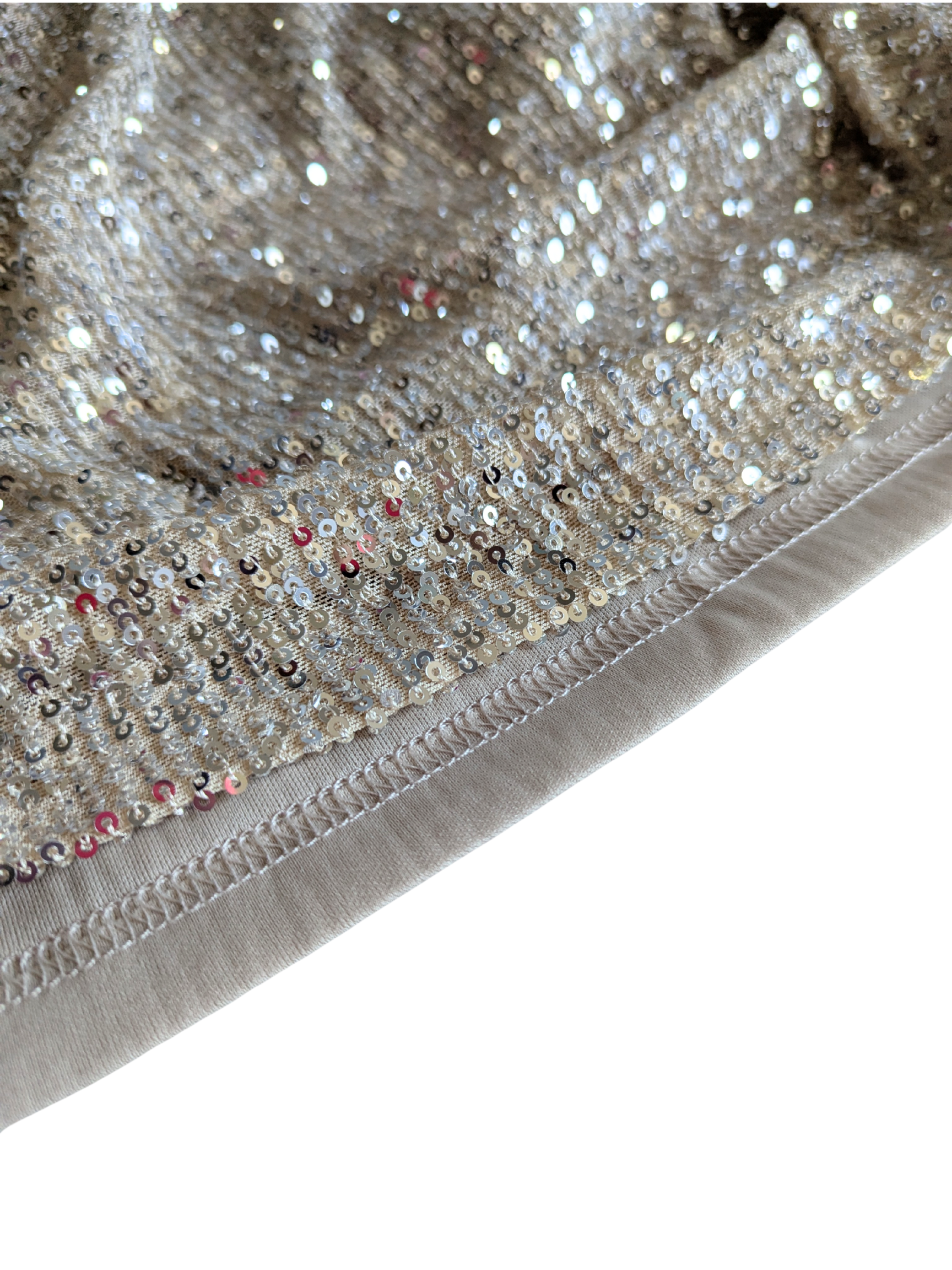 Close-up macro view of the shimmering gold stretch sequin fabric texture and beige stitched hem edge from a curated vintage Betsey Johnson cocktail dress.
