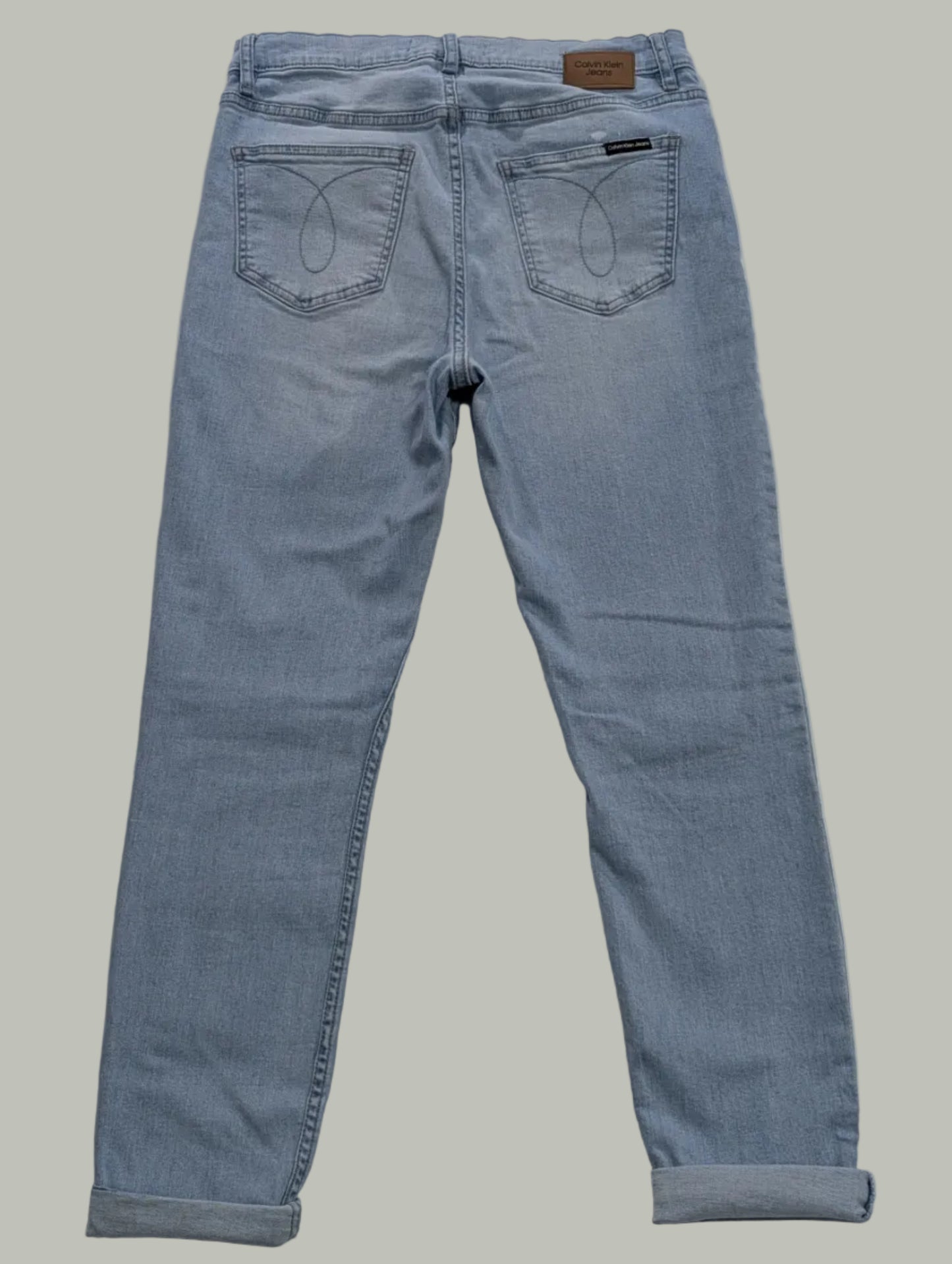 Back full-length view of light wash blue Calvin Klein super skinny jeans with folded cuffed hems, displayed laying flat