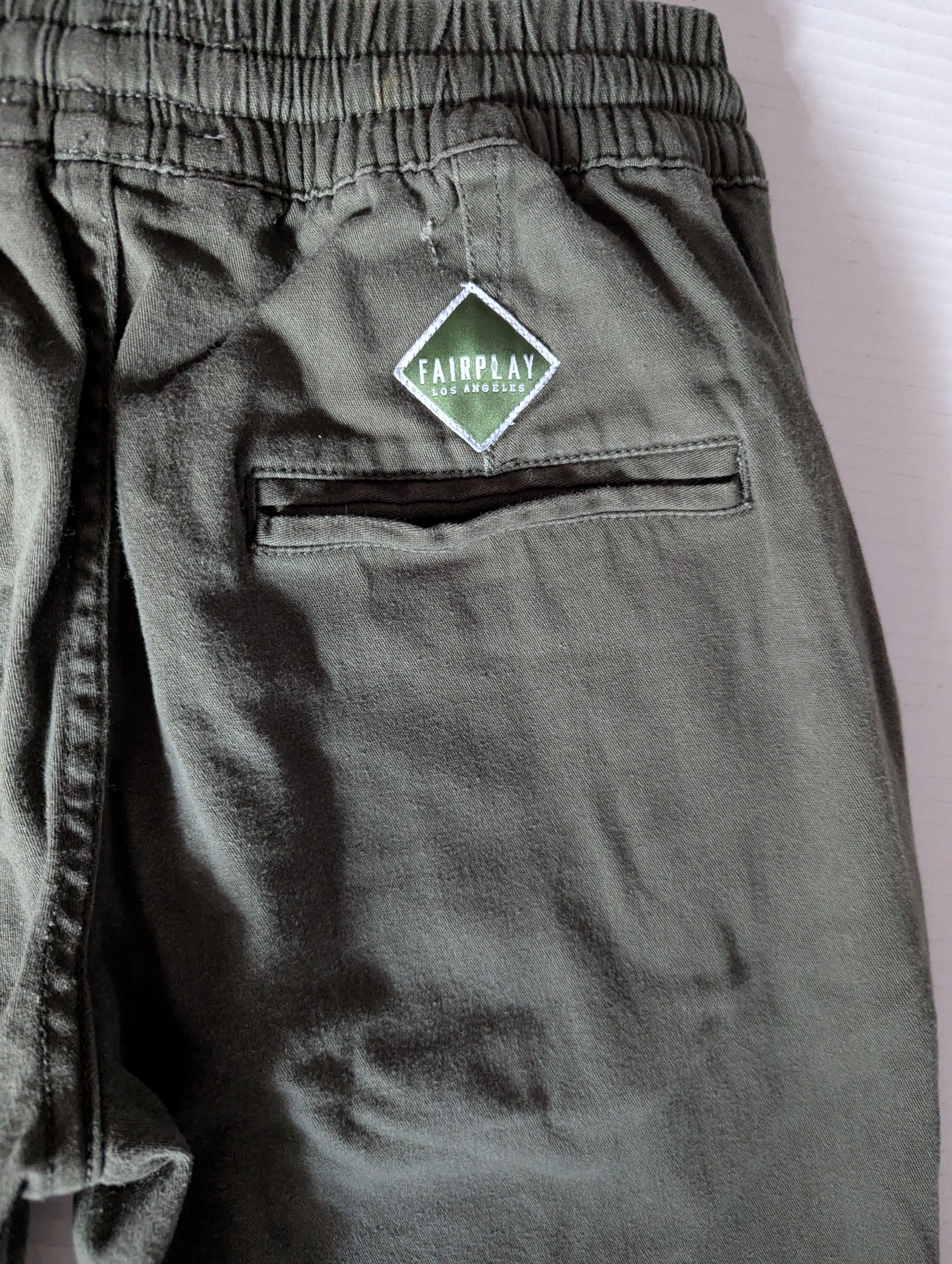Close-up detail of the comfortable elastic waistband and stretch cotton twill fabric on the green Fairplay joggers.