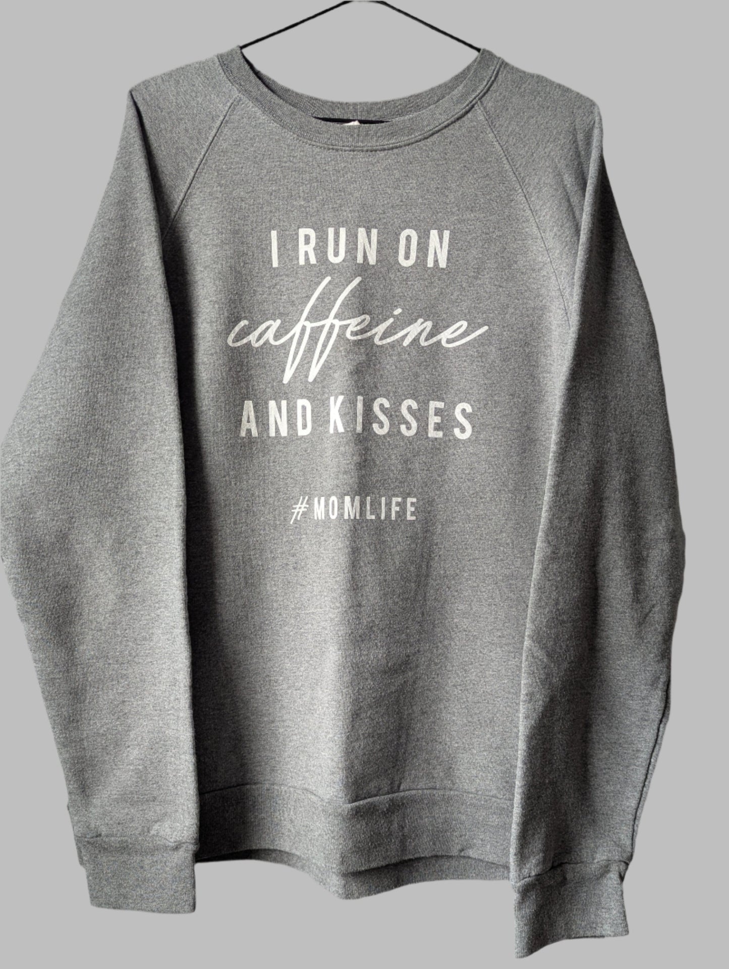 Front view of a heather grey crew neck pullover sweatshirt featuring the white graphic quote I run on coffee and kisses.
