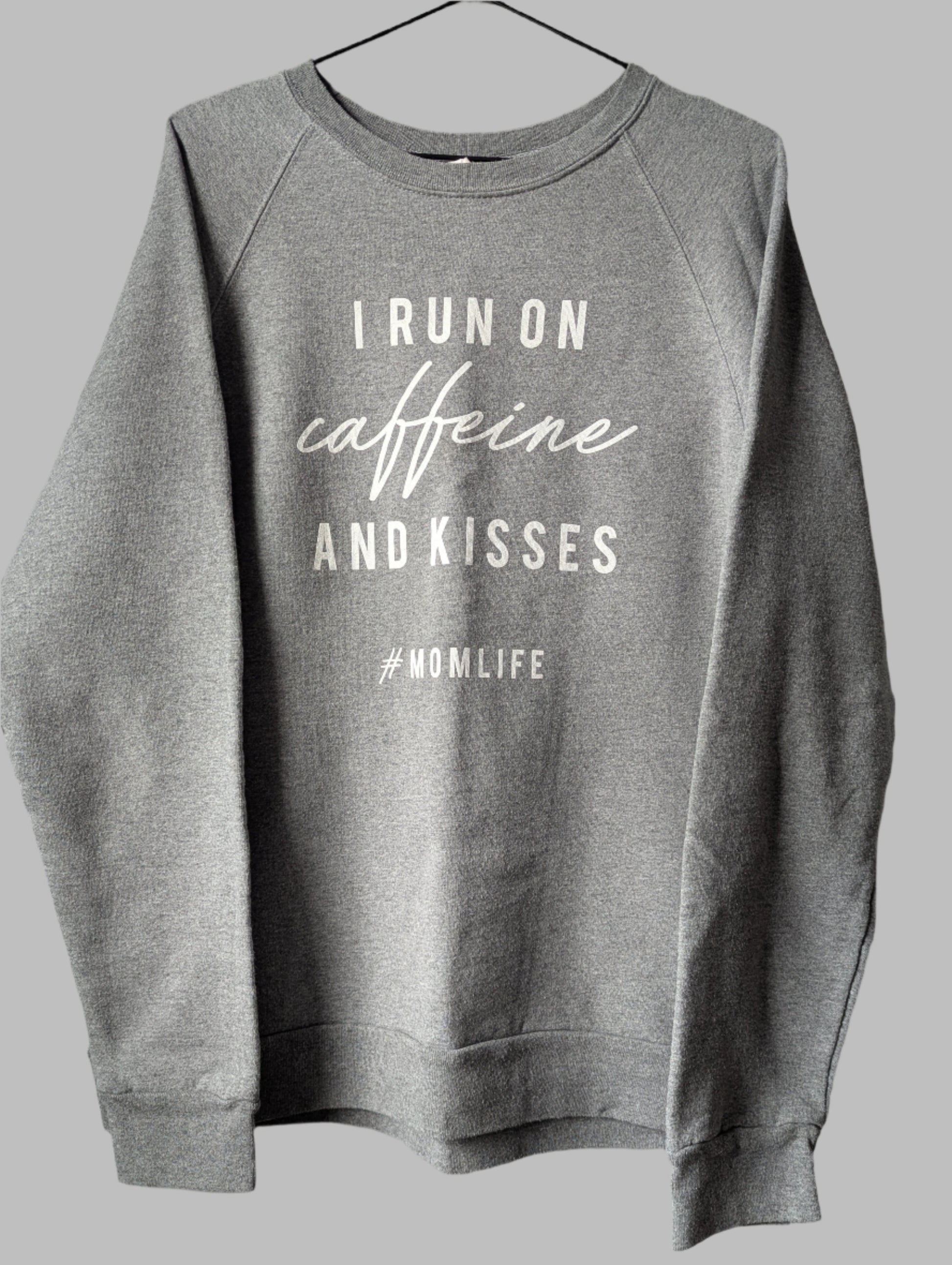 Front view of a heather grey crew neck pullover sweatshirt featuring the white graphic quote I run on coffee and kisses.