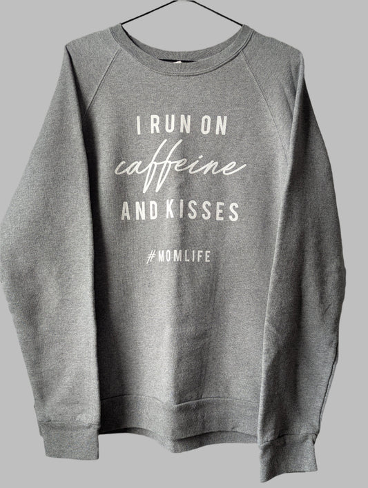 Front view of a heather grey crew neck pullover sweatshirt featuring the white graphic quote I run on coffee and kisses.