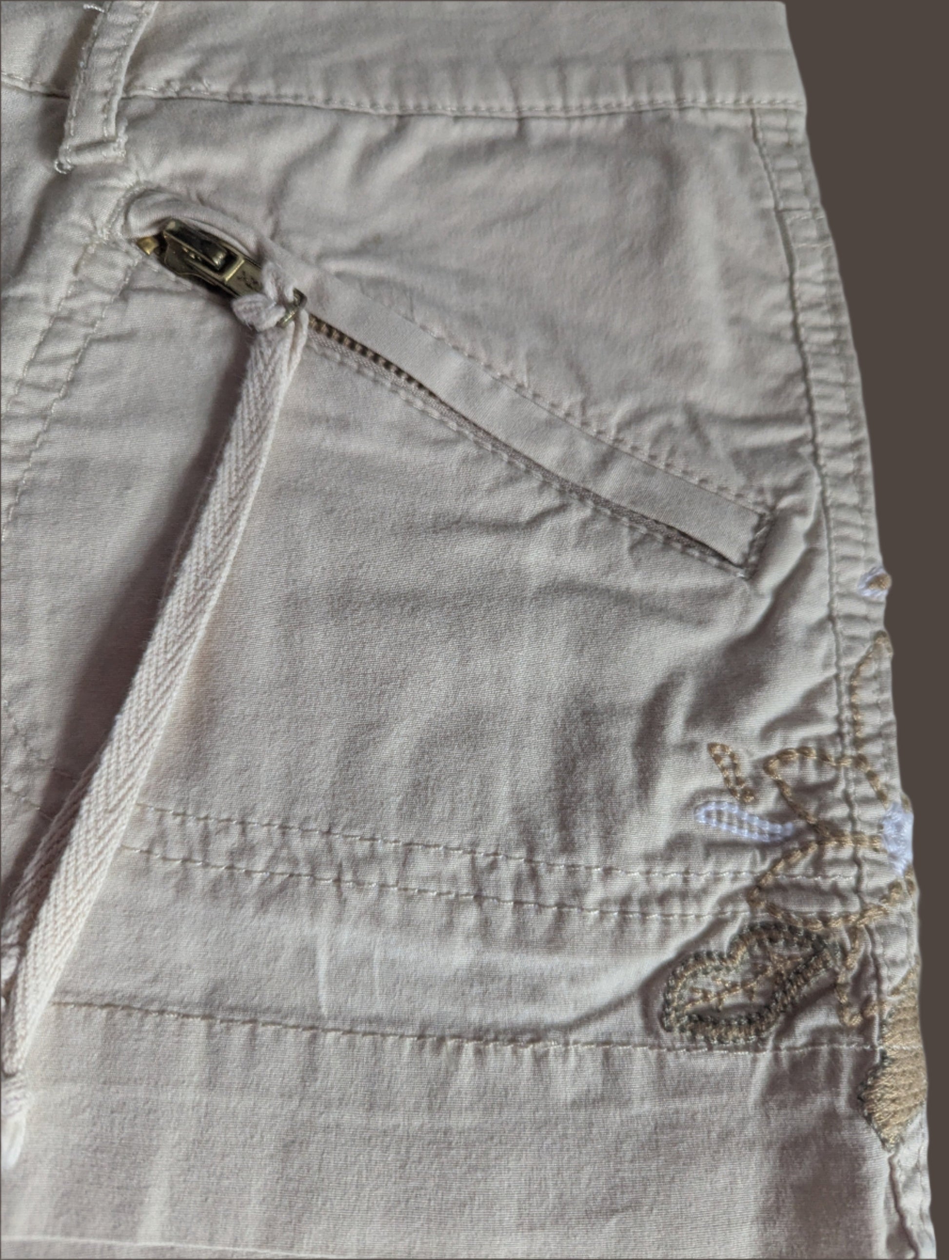 Close-up detail of the intricate embroidery along the waistband and the functional silver front zipper pocket on the Guess shorts.