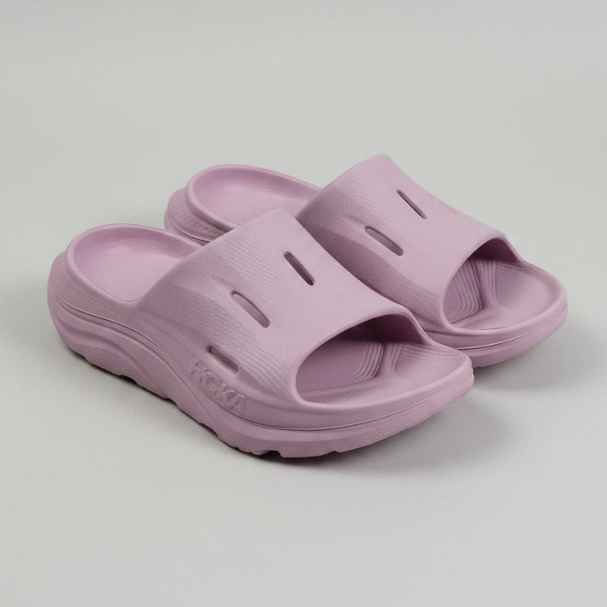 Angled side view of the lightweight, thick-soled lavender Hoka recovery slides, showcasing the cushioned footbed architecture.