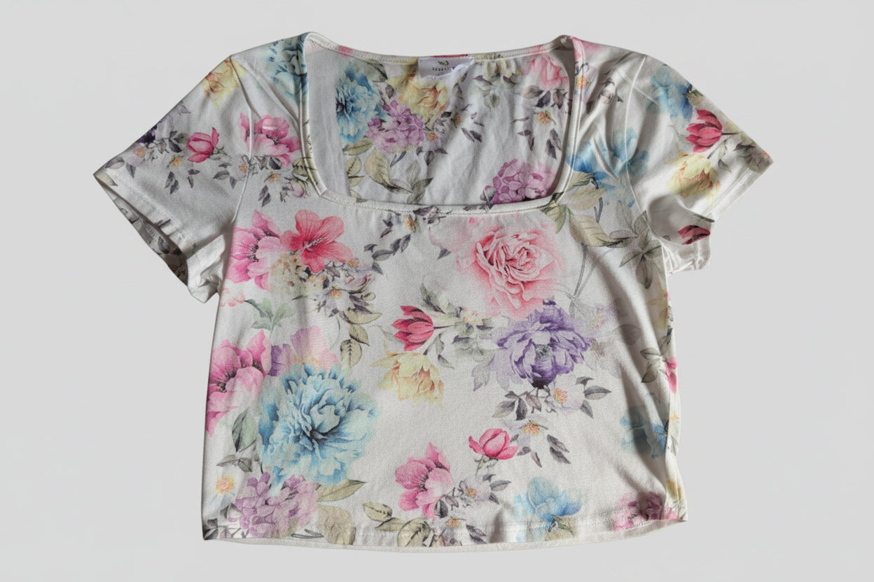 Front view of a white Live in The Moment short sleeve crop top baby tee featuring a colorful all-over pastel floral print.