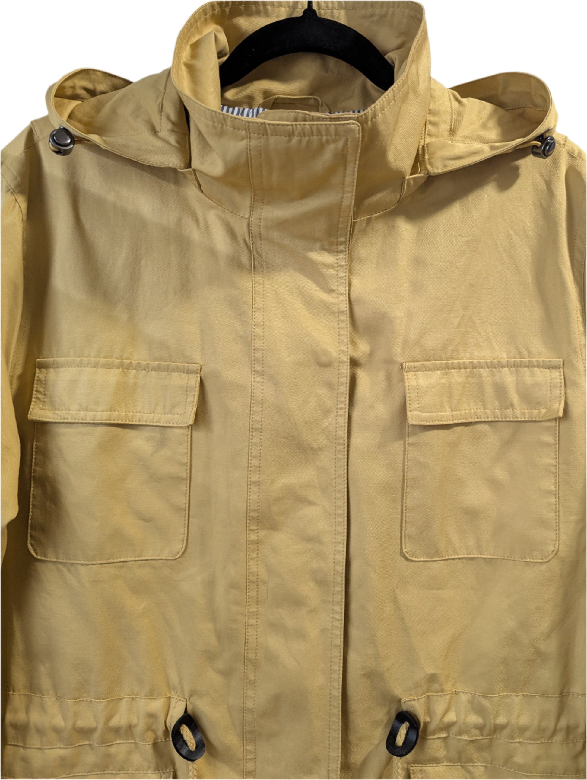 Close-up front view of a mustard yellow London Fog utility jacket, highlighting the collar, detachable hood, snap-button chest pockets, and bottom drawstring grommets