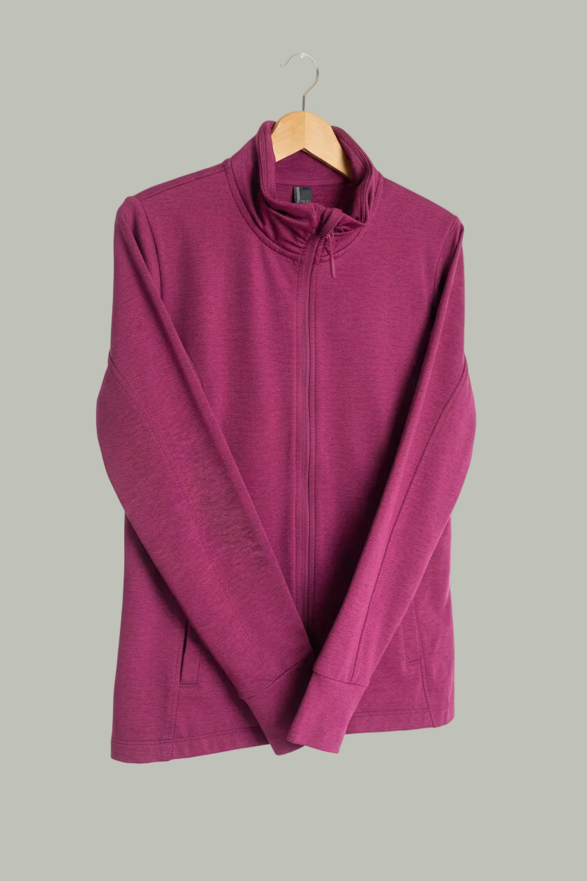 The Mondetta Fuchsia Zip Up Workout Jacket (Size Medium) from Feather & Fable Thrift Co. features a high collar and is displayed on a wooden hanger against a white background.