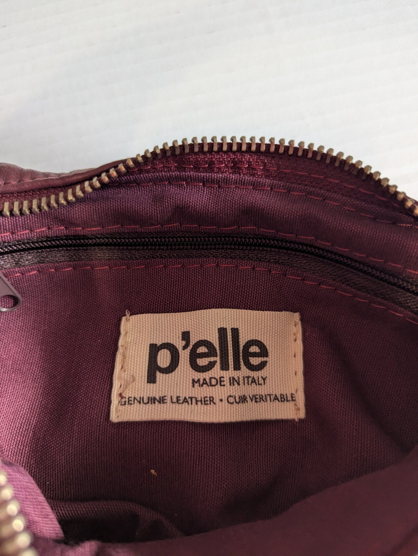Close-up view of the interior authentic P'elle brand logo label inside the maroon purse.