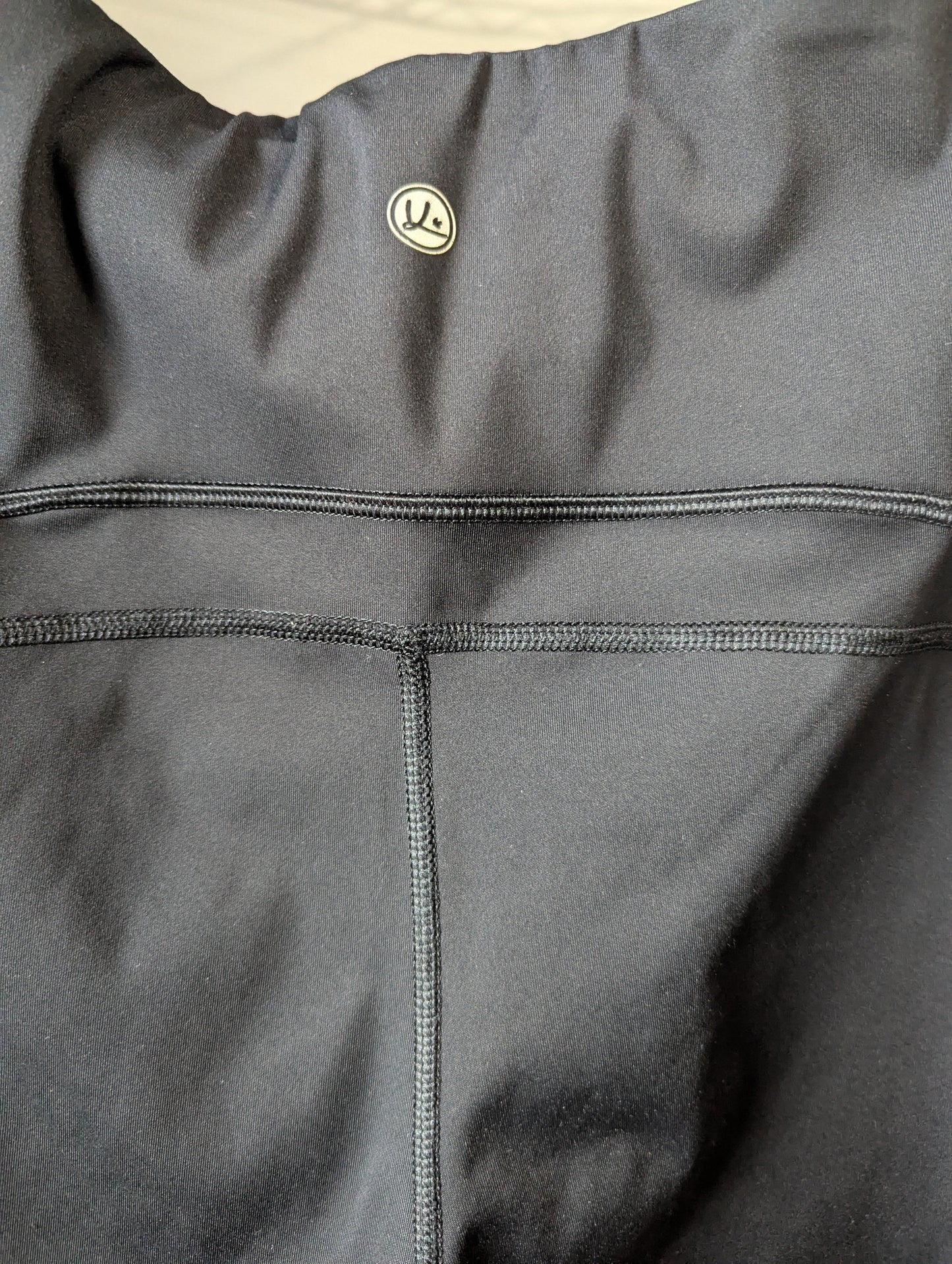 Close-up of the printed authentic Queenie Ke brand logo on the black activewear pants