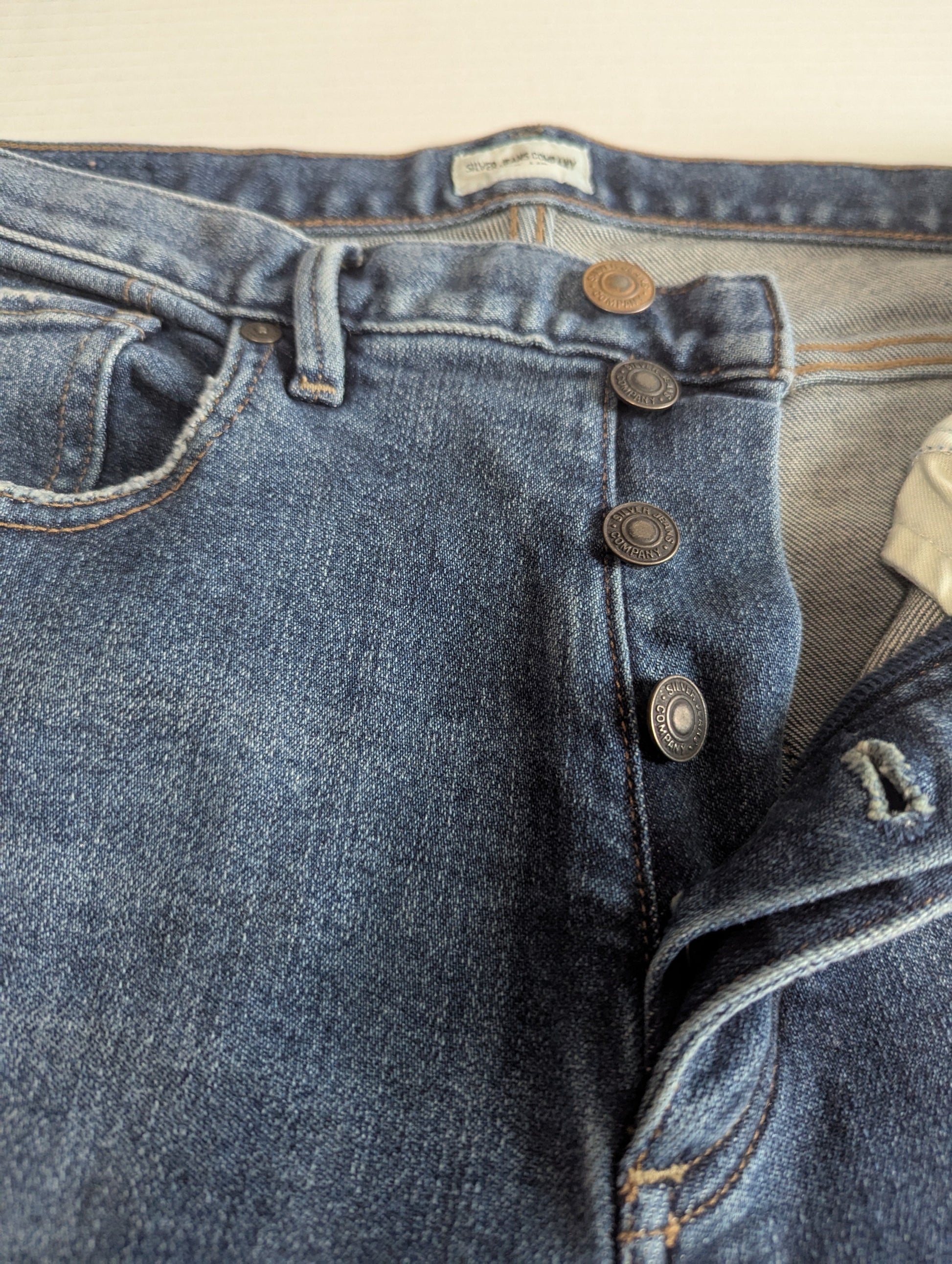 Close-up view of the classic exposed silver button fly closure on the distressed denim jeans.