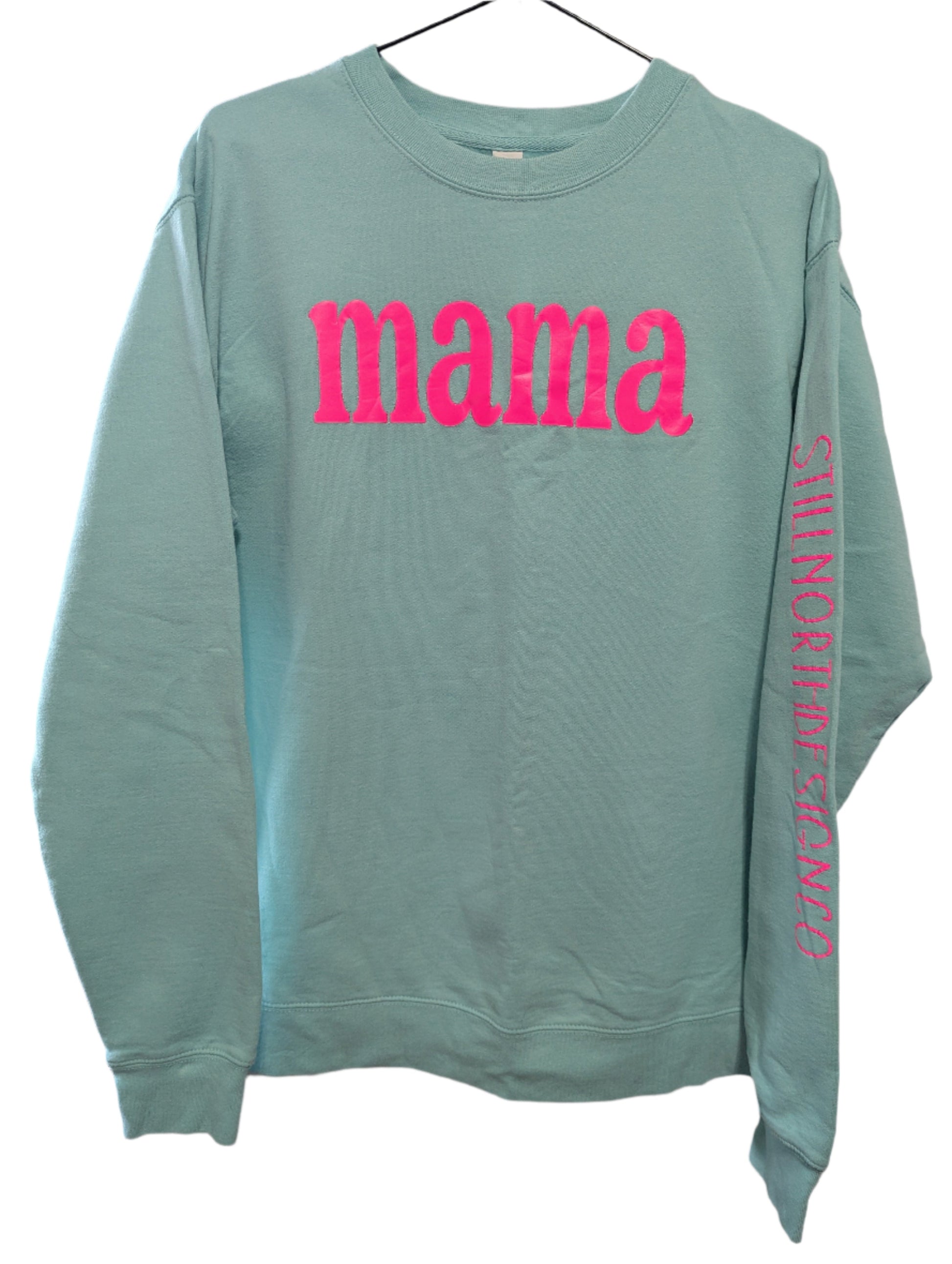 Front view of a teal Still North Design Co MAMA crewneck sweatshirt featuring a bold neon pink graphic print across the front.
