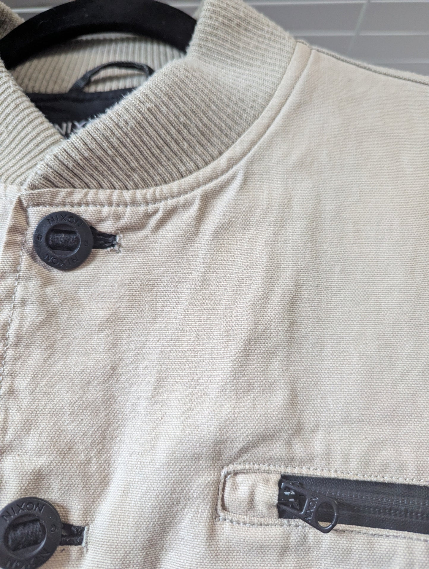 Close-up detail of the ribbed maroon neckline and front metal snap closures on the Nixon University cotton campus jacket.