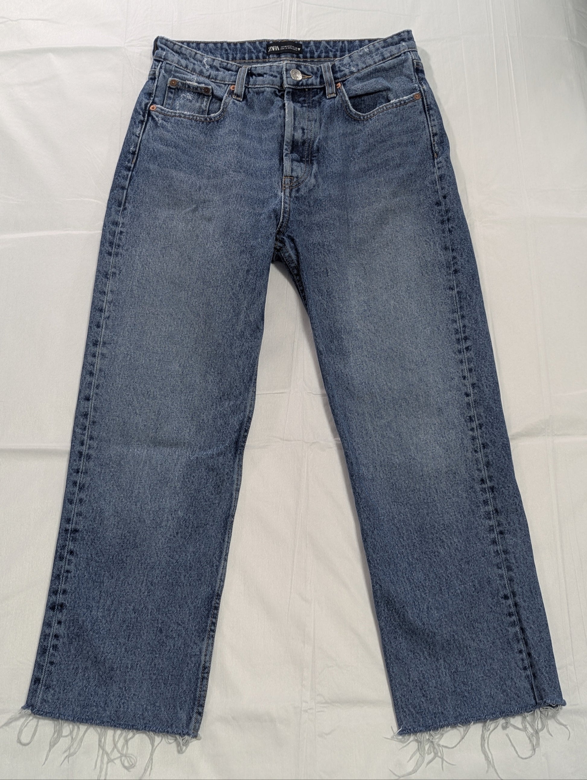 Full-length front view of mid-wash blue Zara high-rise cropped denim jeans with raw frayed hems, displayed flat.
