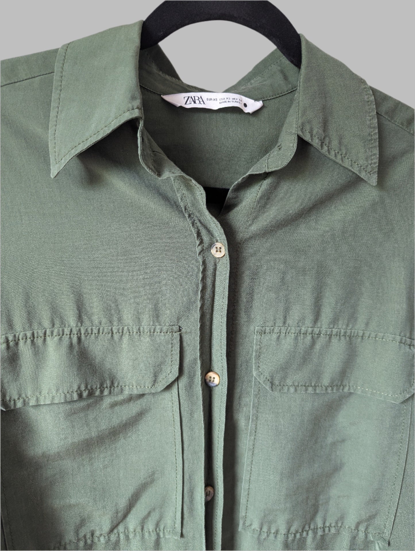 Close-up detail of the collar, button placket, and front flap chest pocket on the green Zara blouse