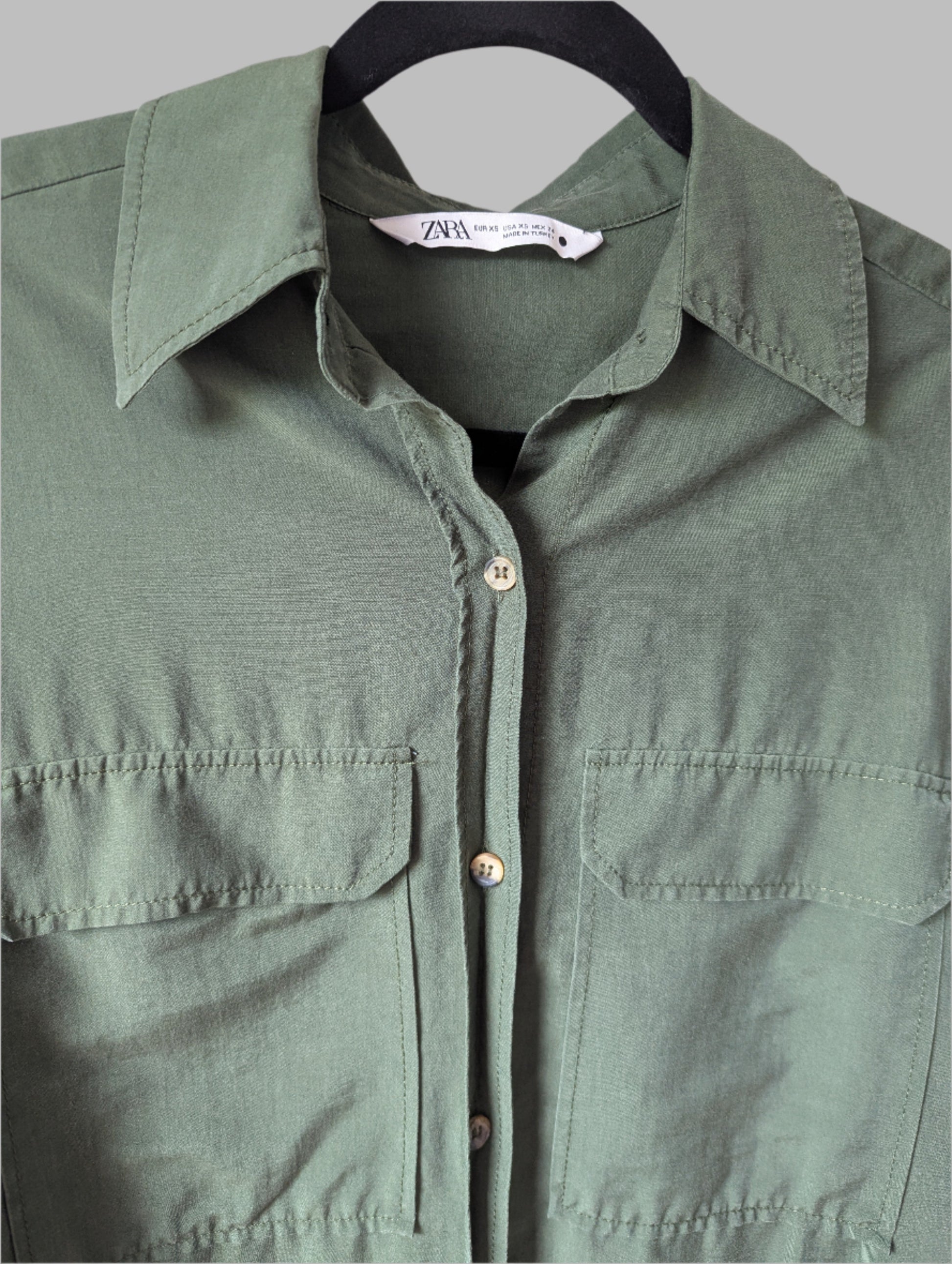 Close-up detail of the collar, button placket, and front flap chest pocket on the green Zara blouse